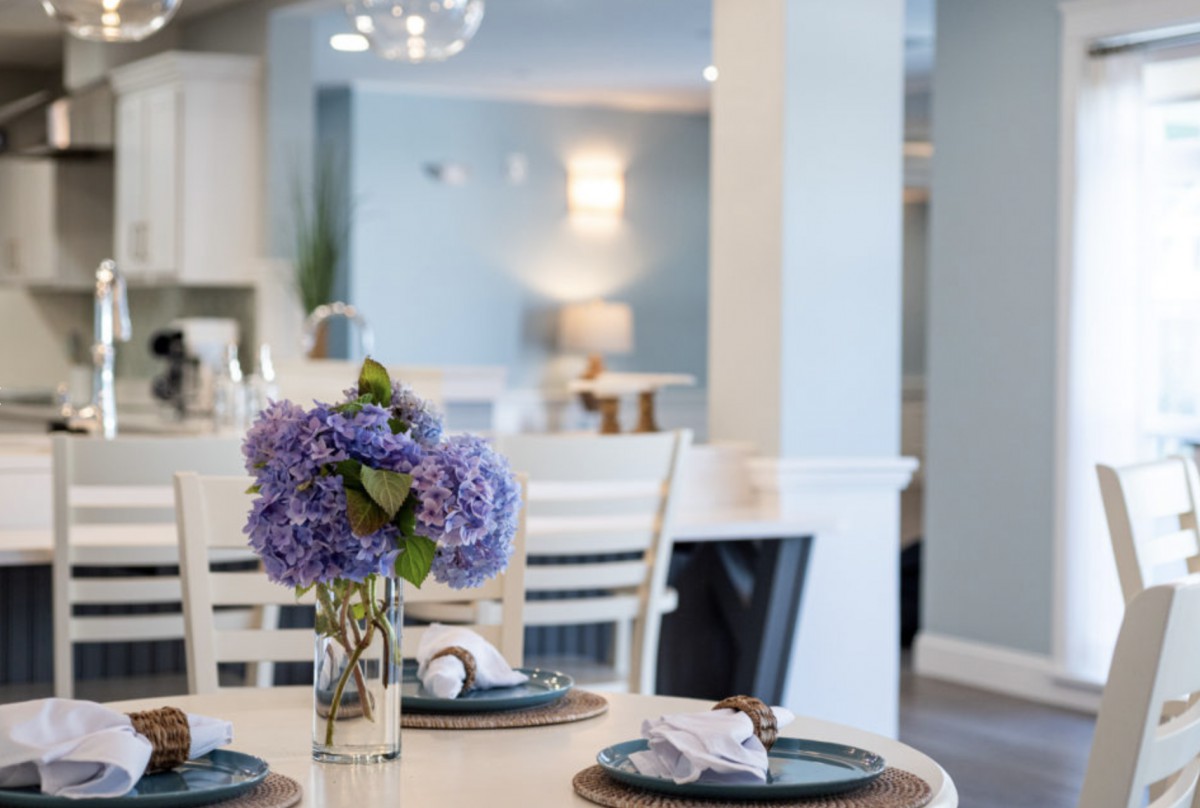 A modern dining area with a vase of purple flowers as the centerpiece, surrounded by elegant table settings.
