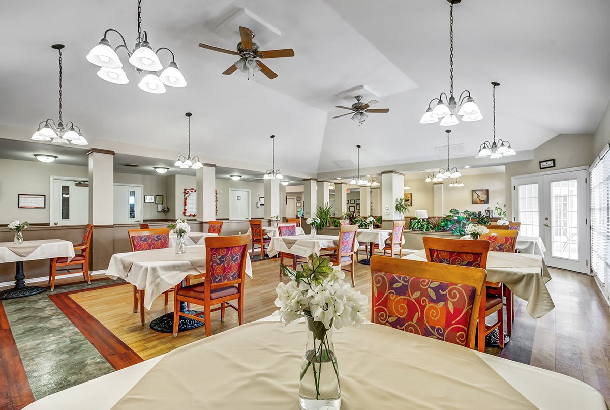 A spacious dining area with neatly arranged tables and chairs, adorned with elegant lighting and ceiling fans.