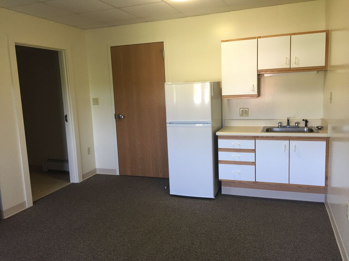 A small kitchen area in an empty apartment with a fridge and sink.