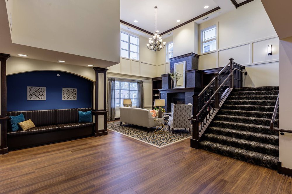 A spacious living room with modern decor, featuring large windows, a chandelier, and wooden flooring.