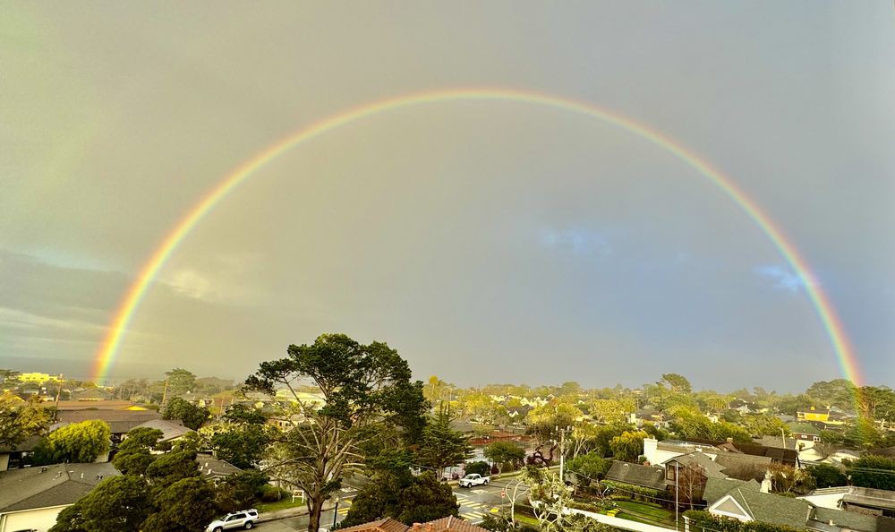 A vibrant rainbow arches over a scenic neighborhood landscape.