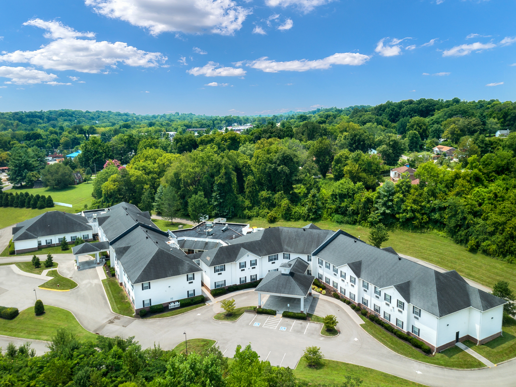 Aerial view of a large residential building surrounded by lush greenery and forest under a bright blue sky.