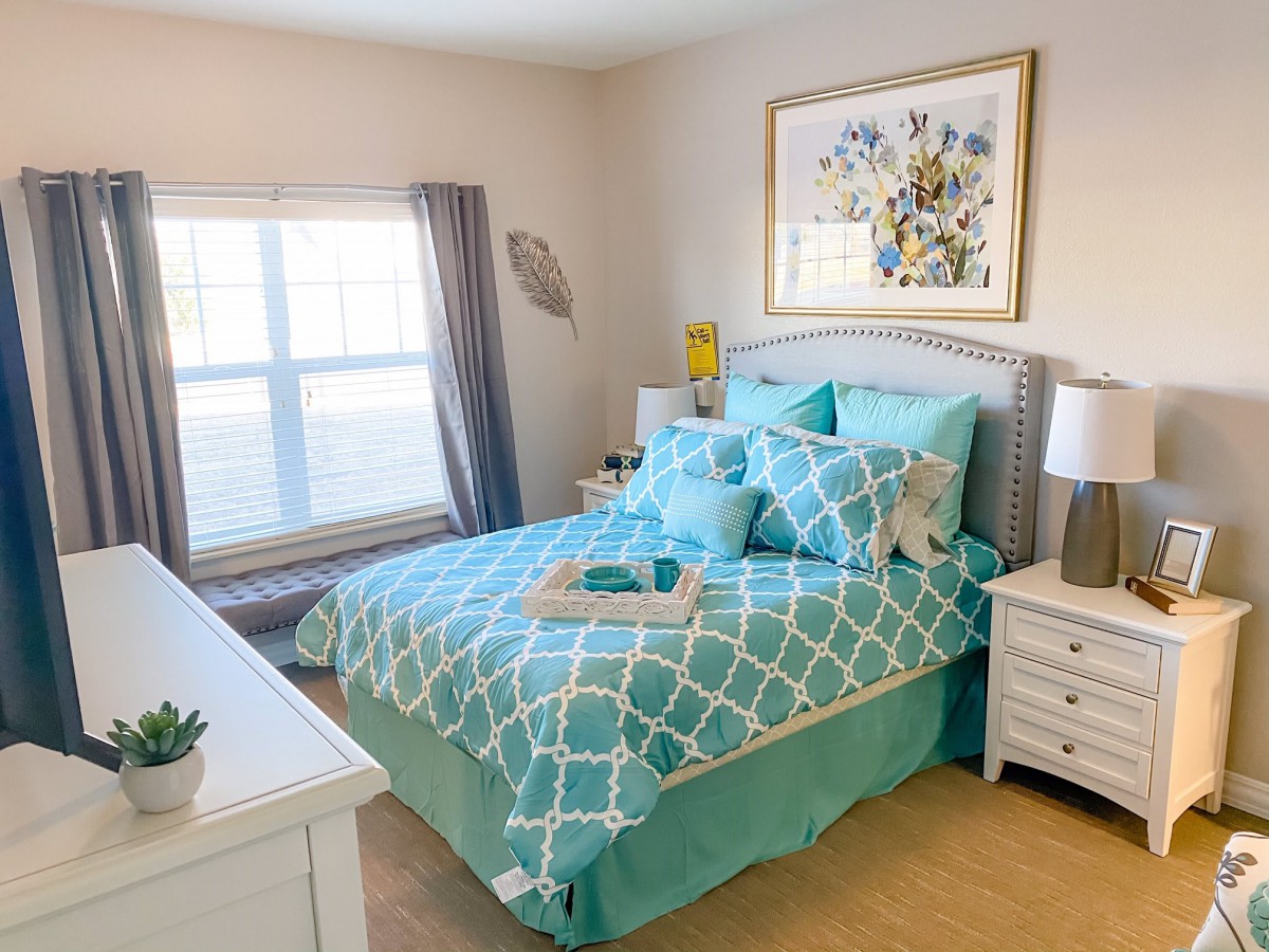A cozy bedroom featuring a turquoise patterned bedspread, with a window letting in natural light and a nightstand on each side of the bed.