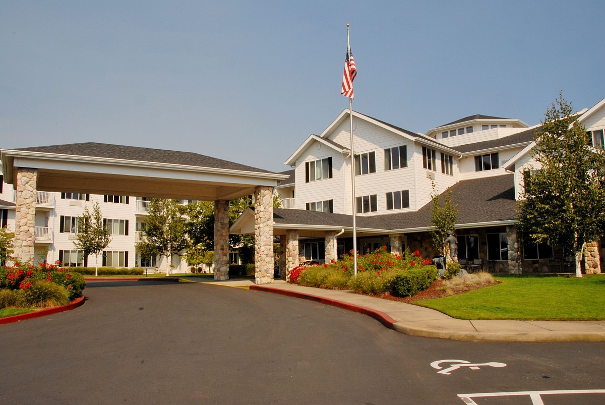 A multi-story residential building with an American flag and a landscaped driveway.