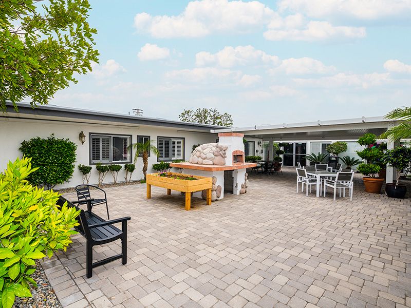 A spacious outdoor patio with a brick oven, seating area, and paved flooring.