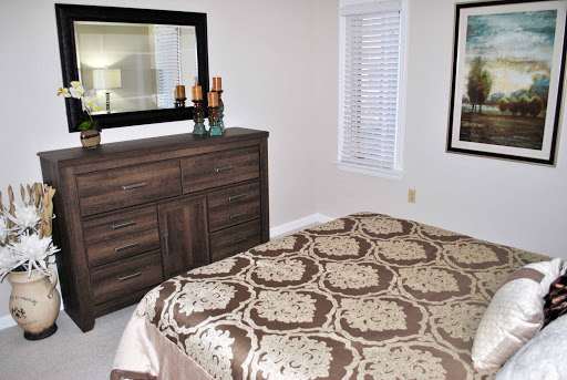 A cozy bedroom featuring a patterned bedspread, wooden dresser, and decorative mirror.