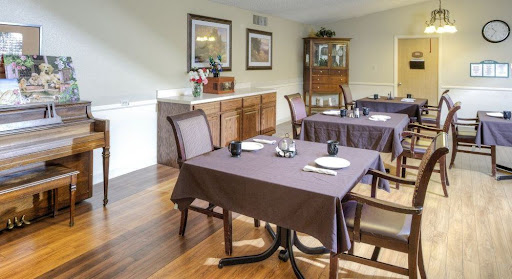 A cozy dining room setup featuring wooden tables and chairs with brown tablecloths, complemented by wall decorations and a decorative cabinet.