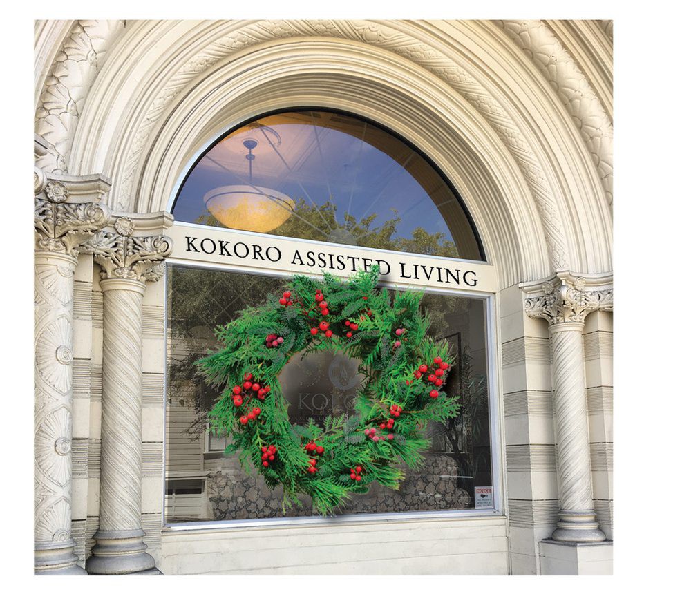 An arched window of 'Kokoro Assisted Living' adorned with a festive holiday wreath.