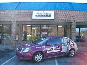 A branded car parked in front of a storefront displaying the Home Instead Senior Care logo.