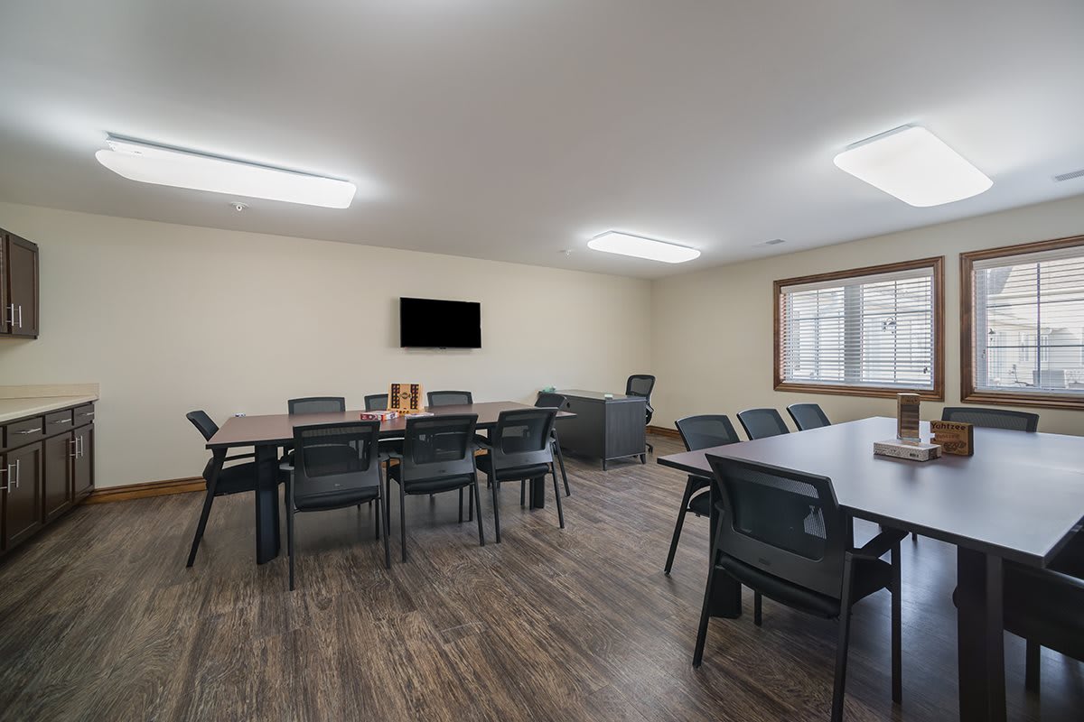 A modern conference room with tables, chairs, and a wall-mounted TV.