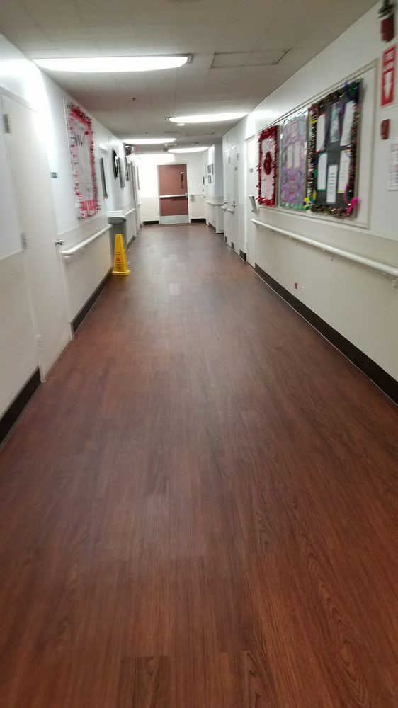 A clean hospital corridor with wooden flooring and various notices on the walls.