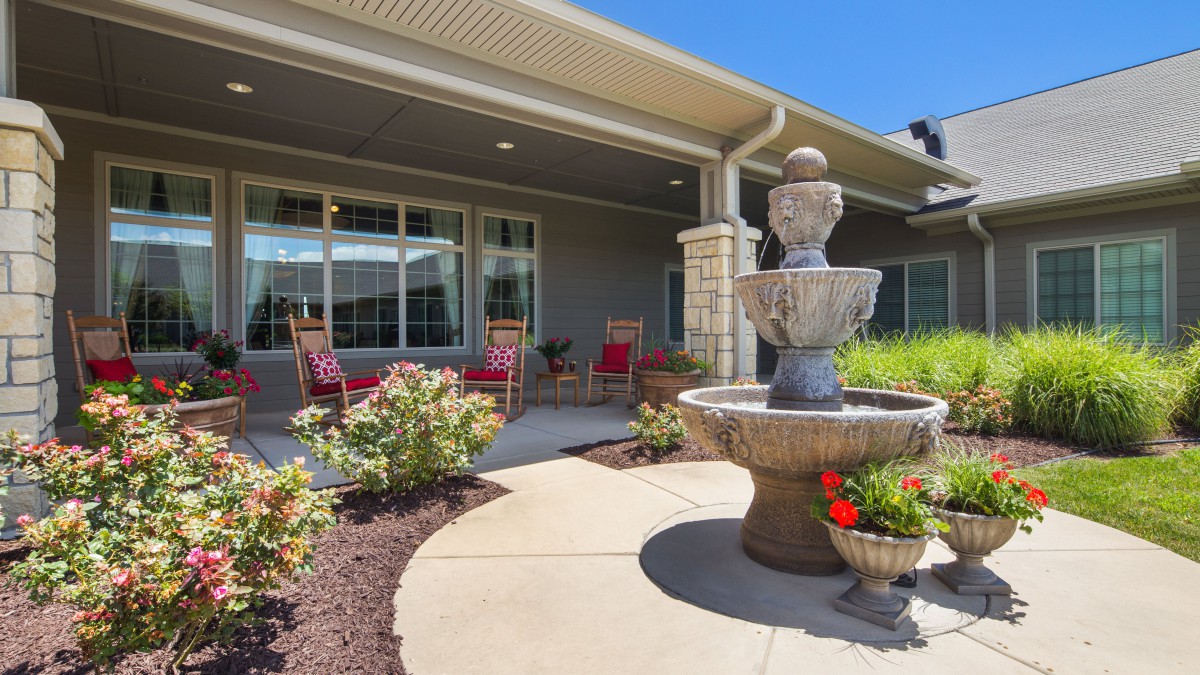 A sunny patio with a decorative fountain, surrounded by flowers and comfortable seating.