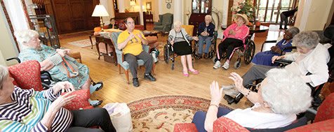 A group of elderly individuals sitting in a circle during a social gathering in a living room setting.