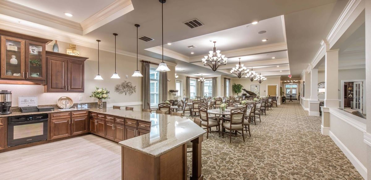 An elegant dining area featuring multiple tables and chairs, adorned with chandeliers and a carpeted floor.