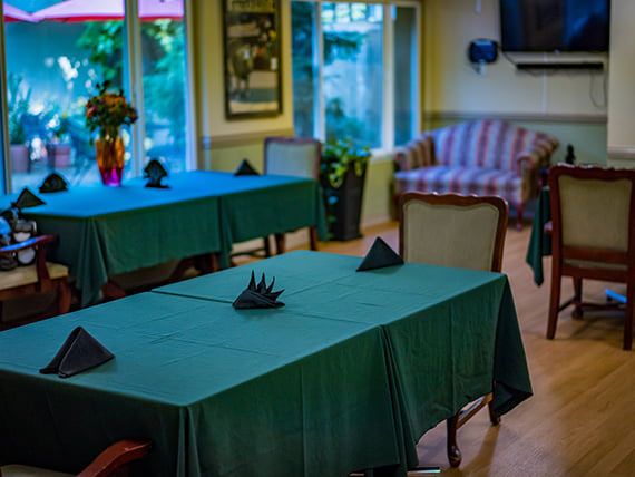 A cozy restaurant dining area with tables covered in green tablecloths, neatly folded napkins, and comfortable seating.