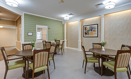 A neatly arranged dining area with several tables and chairs, featuring green walls and artwork.