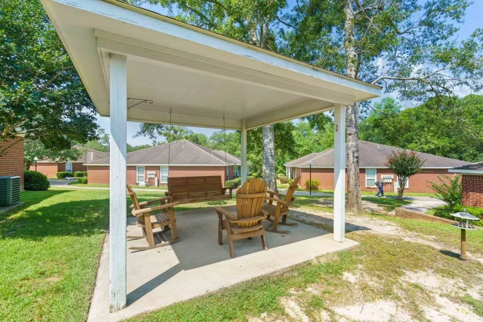 A cozy backyard gazebo features a wooden swing and chairs for outdoor relaxation.