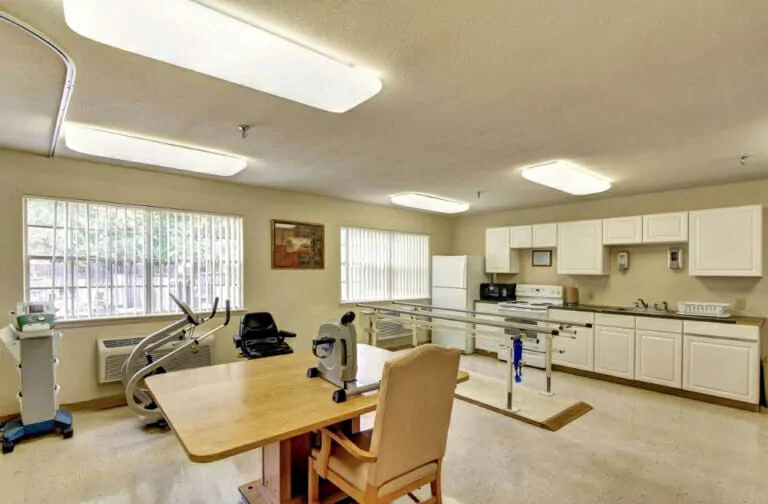 A rehabilitation room equipped with exercise machines and a kitchen area for physical therapy exercises.