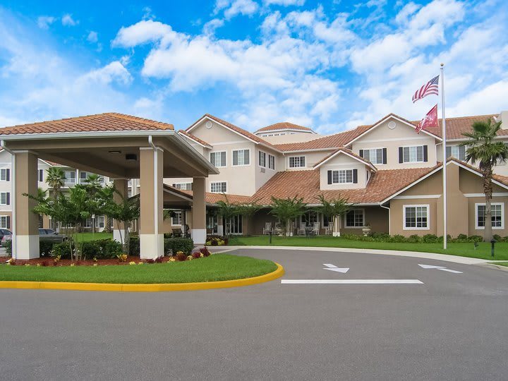 A well-maintained residential building with an entrance driveway and flags flying against a partly cloudy sky.