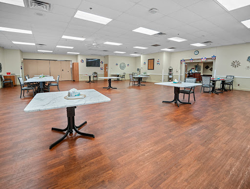 A spacious and well-lit indoor dining area featuring several empty tables on a wooden floor.