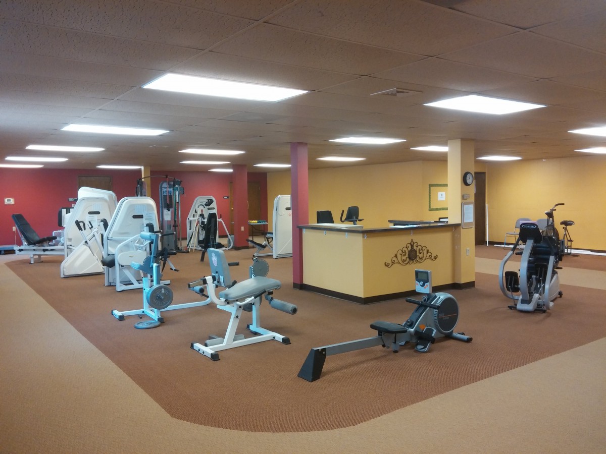 A well-lit gym with various exercise machines and a reception desk.