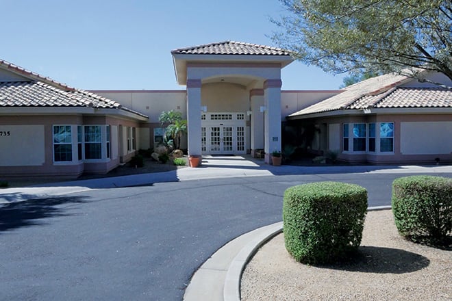 A building entrance with a landscaped driveway and neatly trimmed bushes.