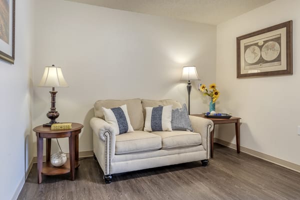 A cozy living room with a beige sofa, accented by blue and white cushions, flanked by two wooden tables and lamps.