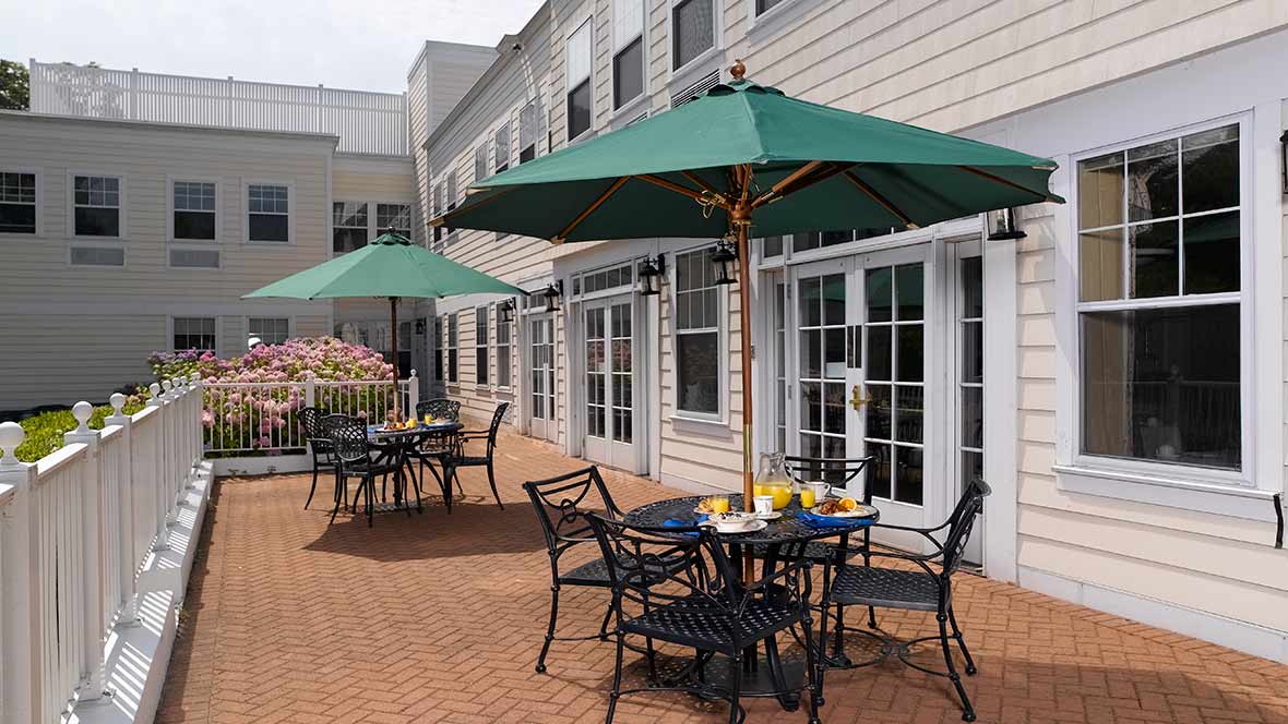 An outdoor restaurant patio with tables, chairs, and umbrellas on a brick surface.