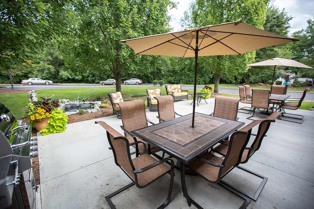 A well-furnished patio with a table, chairs, and umbrellas in a garden setting.