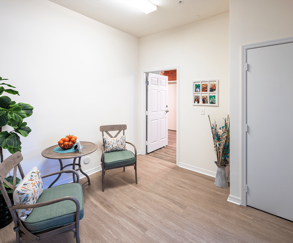 A cozy waiting room with chairs and a small table, decorated with plants and art on the wall.