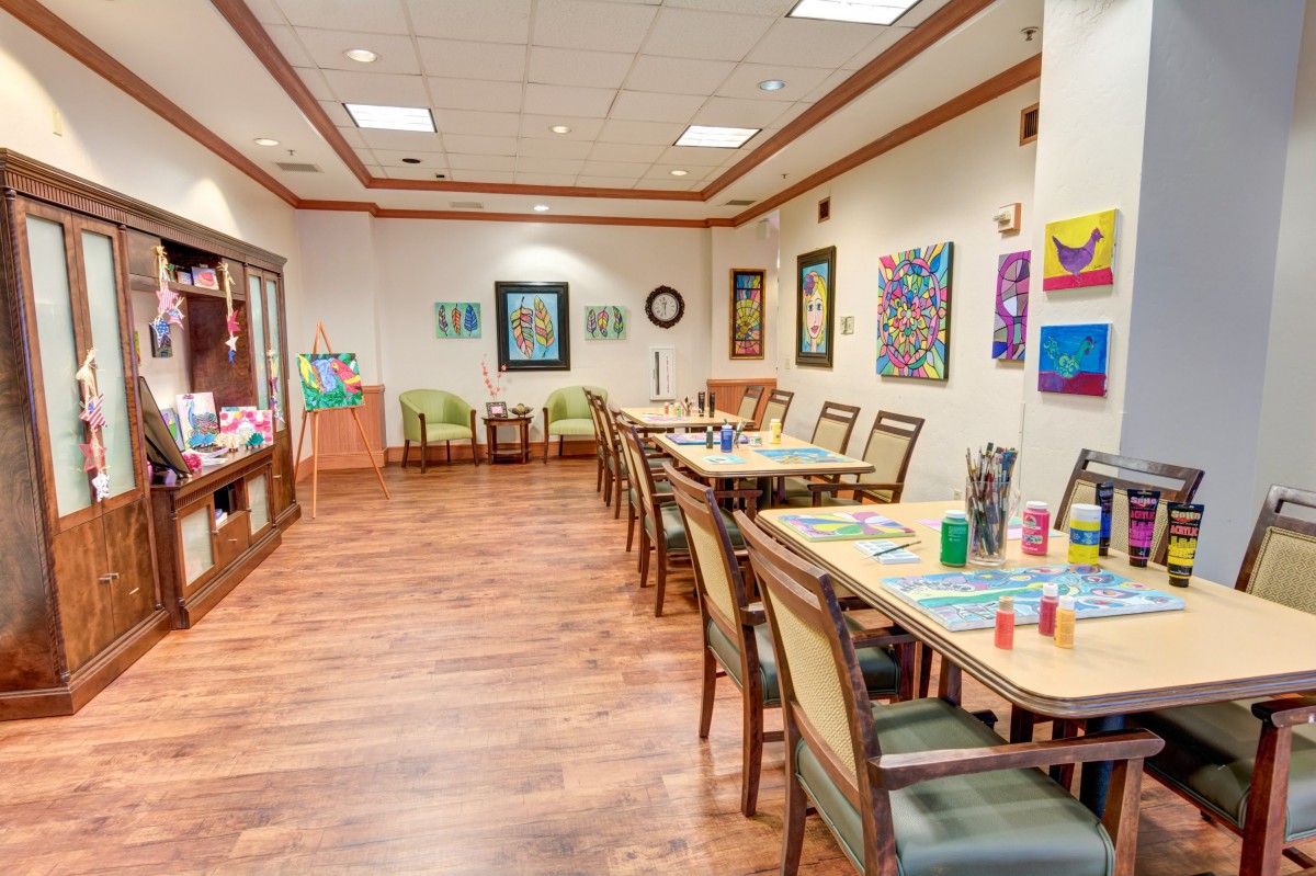 A bright art room with tables, chairs, and various painting supplies.