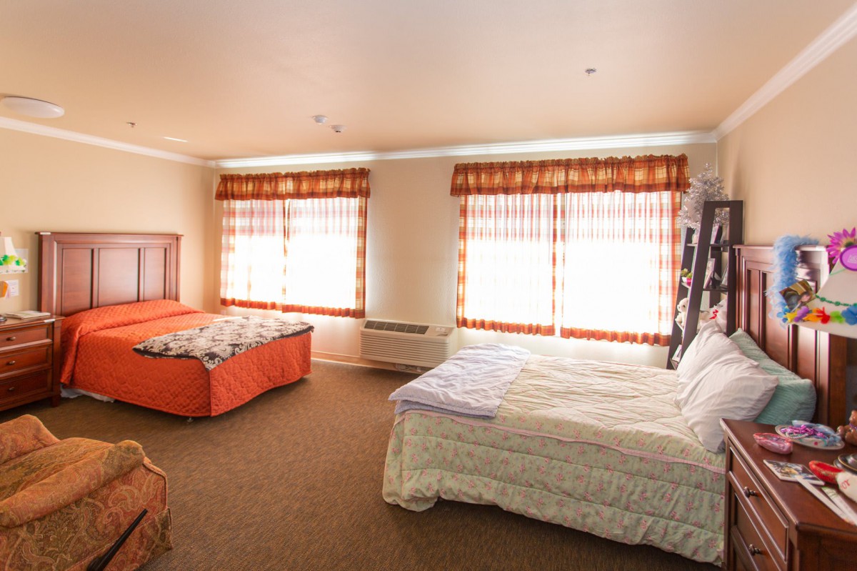 A spacious hotel room with two beds and large windows adorned with curtains.
