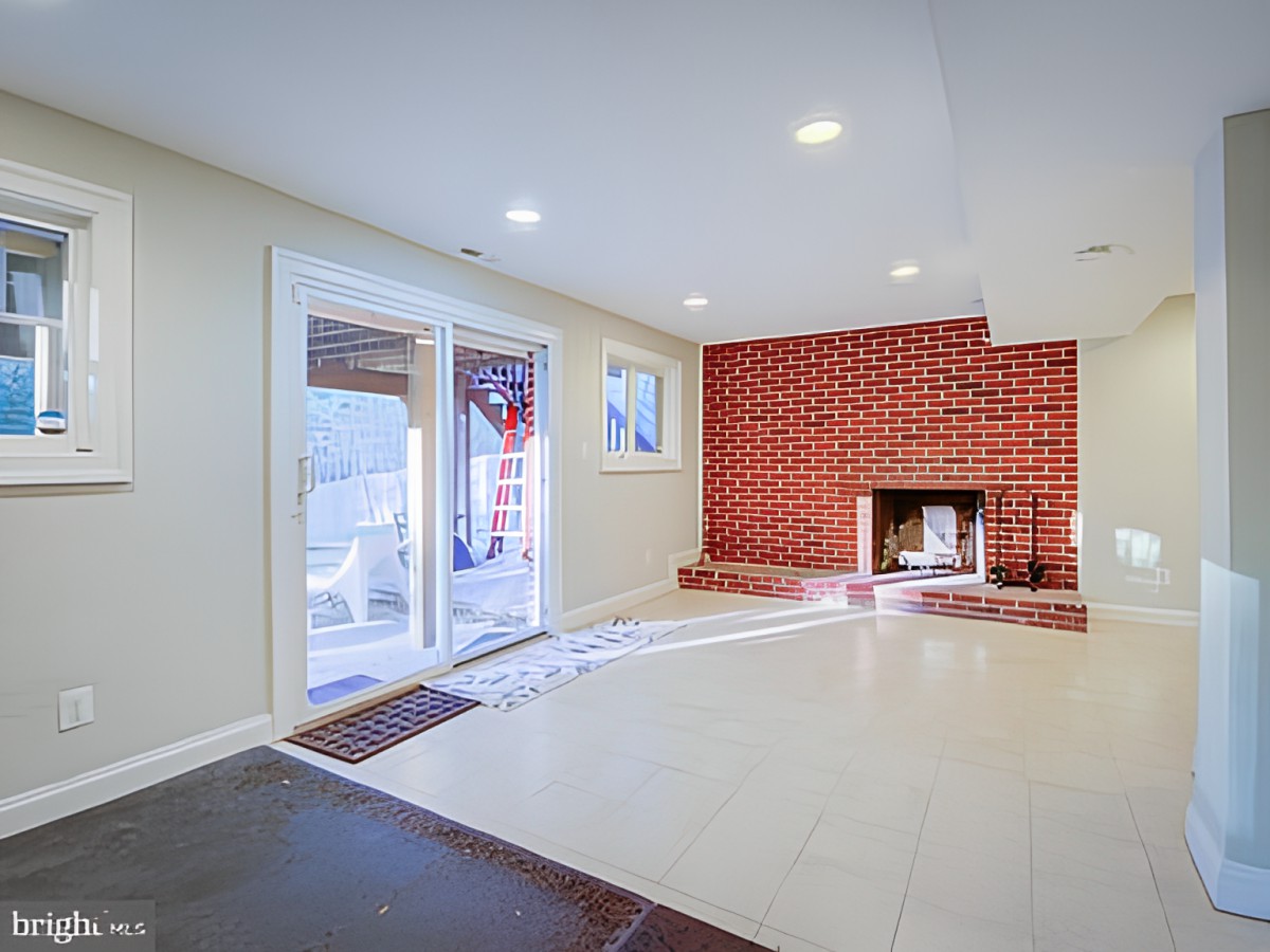 A spacious living room featuring a brick fireplace, large windows, and tile flooring.
