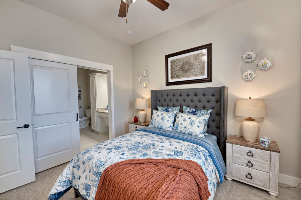A cozy bedroom featuring a queen-sized bed with floral bedding, flanked by nightstands with lamps, and a ceiling fan overhead.