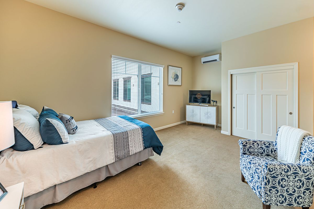 A minimalist bedroom featuring a neatly made bed, television, and large window.