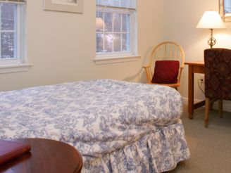 A cozy bedroom with a bed, chair, and lamp near a window.