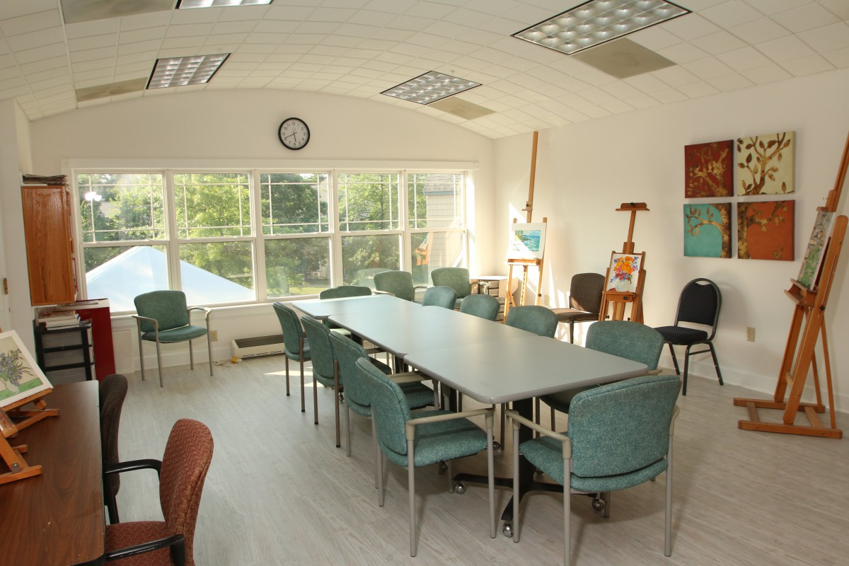 A bright meeting room with a long conference table, several chairs, and windows allowing natural light.