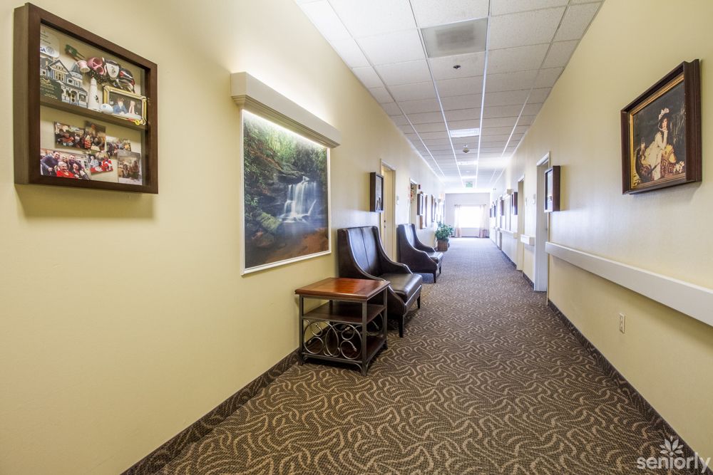 A hallway with chairs and tables along the wall, featuring carpeted flooring and artwork on the walls.