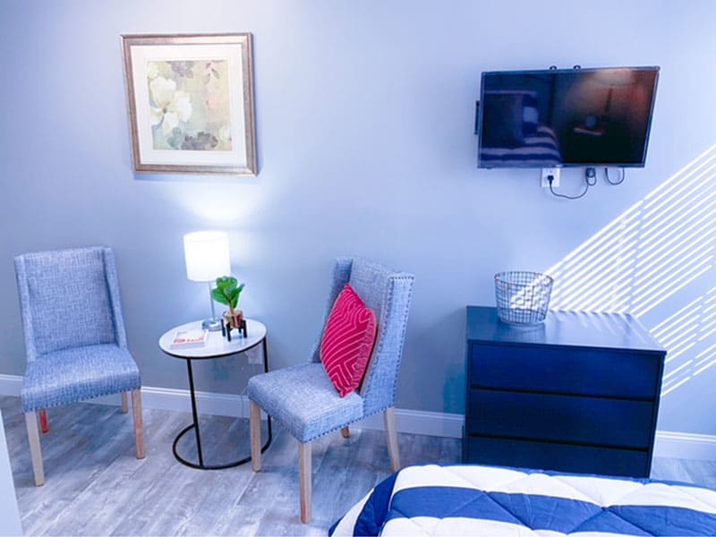 A modern bedroom interior with chairs, a small table, and a wall-mounted TV.
