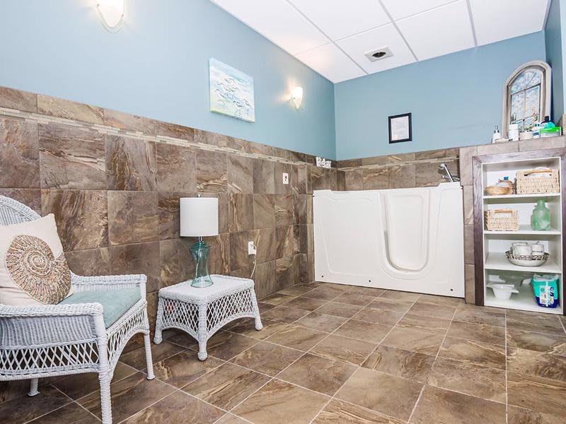 A spacious bathroom with a walk-in tub, featuring tile walls and floor, light blue walls, and wicker furniture.