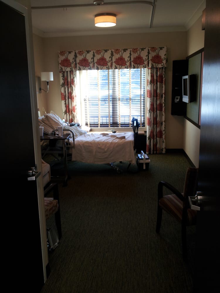 A hospital room with a bed and medical equipment near a window.