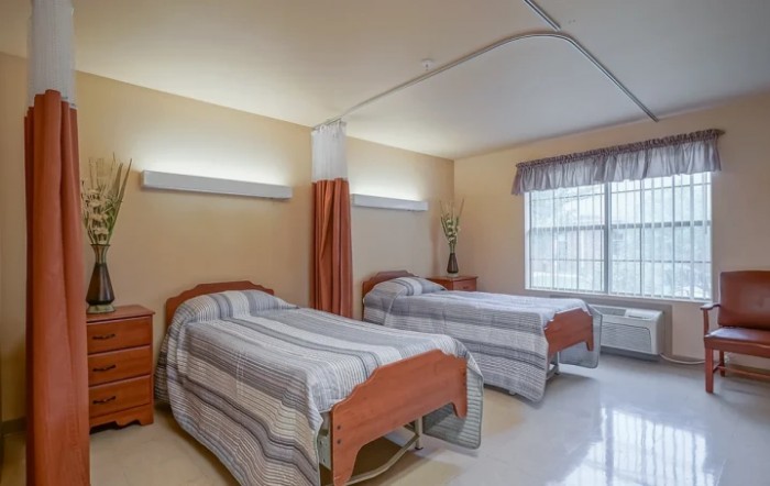A hospital room with two neatly made beds and a curtain divider.