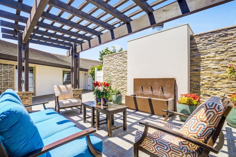 A stylish patio with comfortable seating under a pergola, adorned with colorful cushions and decorative flowers.