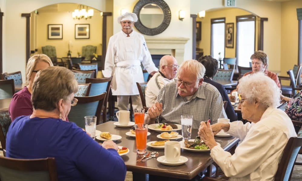 A group of seniors enjoying a meal at a restaurant with the chef nearby.