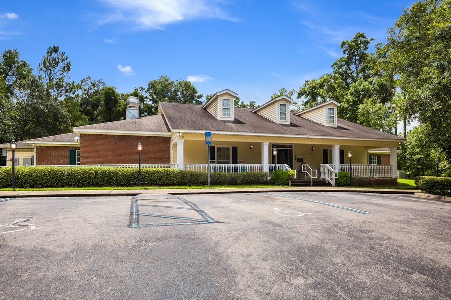 A single-story house with a parking lot in front, surrounded by trees under a blue sky.