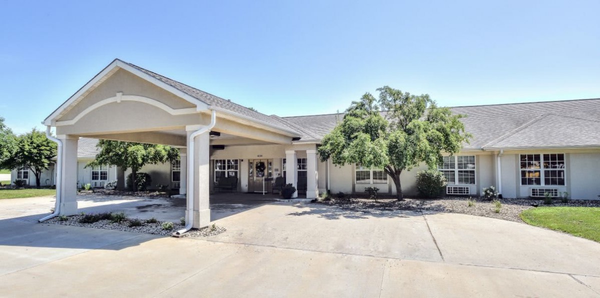 A building entrance with a covered driveway and surrounding trees.