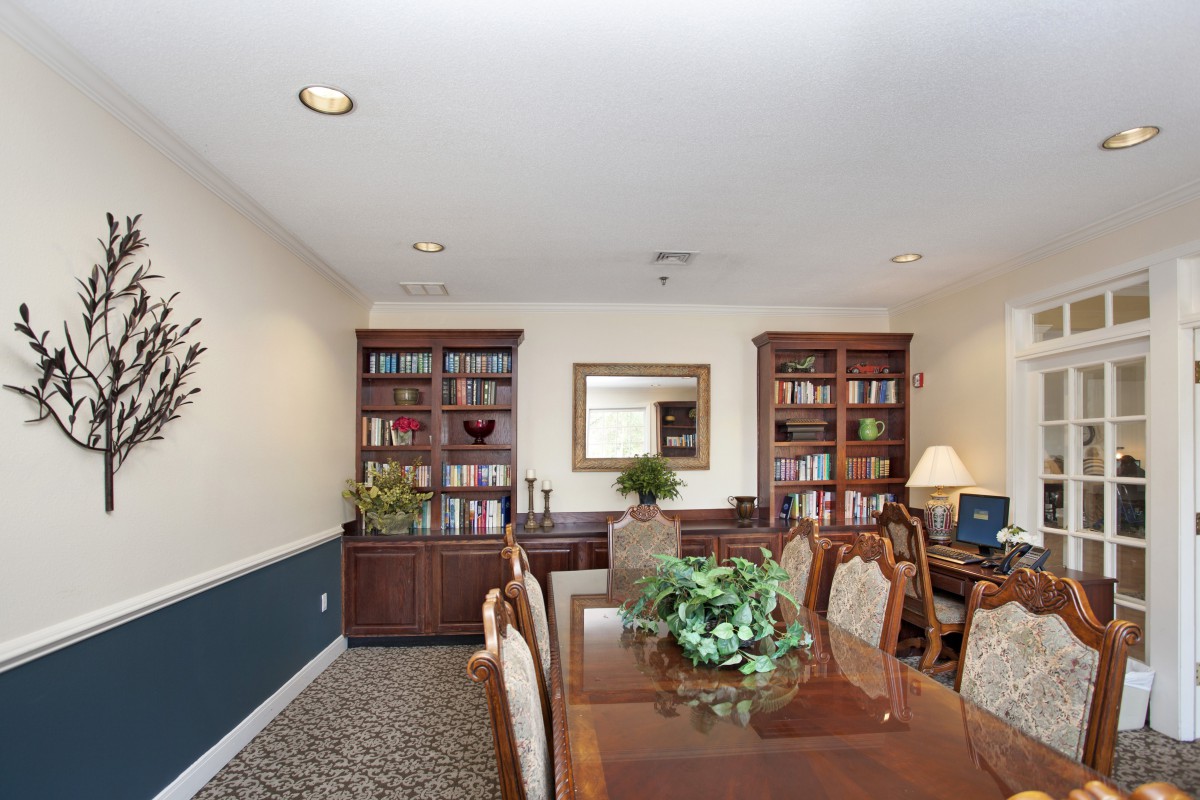 A well-organized office conference room with bookshelves and a large wooden table surrounded by chairs.
