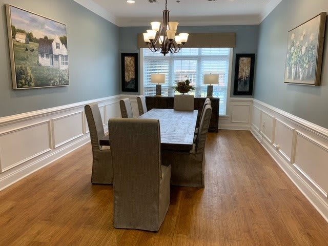 A well-decorated dining room featuring a long table, cushioned chairs, a chandelier, and large windows.
