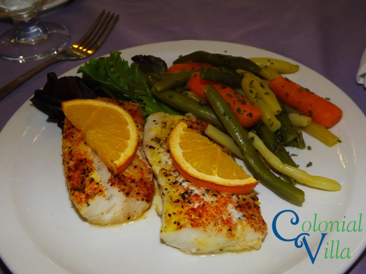 A delicious plate featuring seasoned fish with citrus garnish, accompanied by a medley of mixed vegetables.