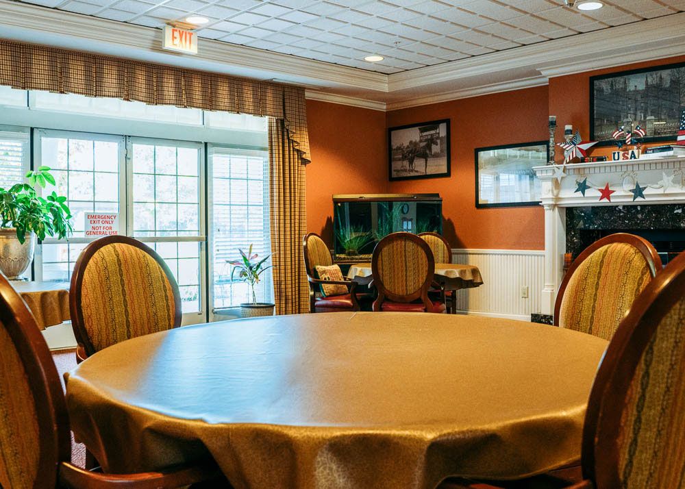 A cozy dining room with a round table and chairs, featuring warm decor and large windows.